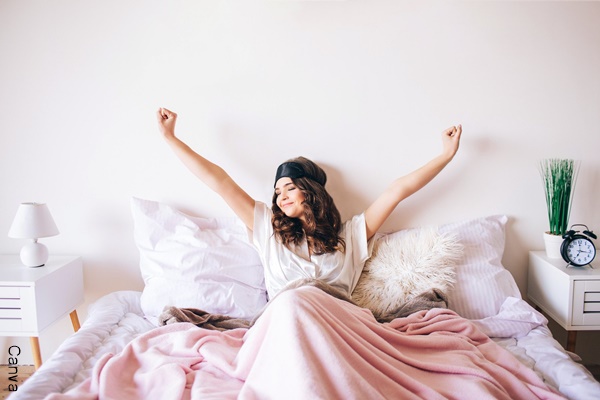 Foto de mujer sonriendo y extendiendo los brazos en la cama.