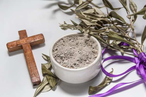 Ceniza de cuaresma con una cruz de madera y una palma con una cinta morada al fondo