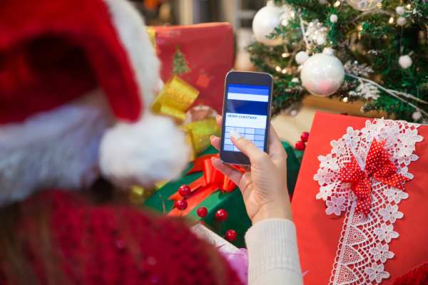 Persona con ropa navideña utilizando su teléfono frente a algunos regalos de navidad