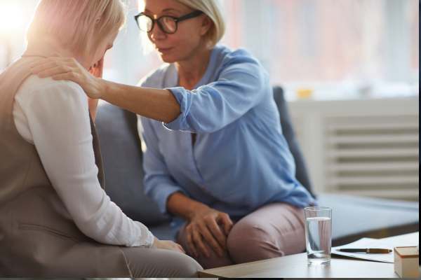 Foto de plano general de una señora consolando a otra mujer y cogiéndole el hombro