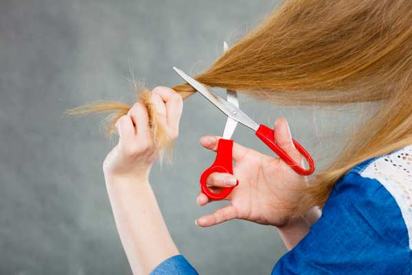 Mujer cortándose el cabello con tijeras rojas