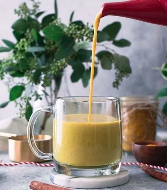 Imagen de una mesa encima un vaso en donde están sirviendo leche dorada 