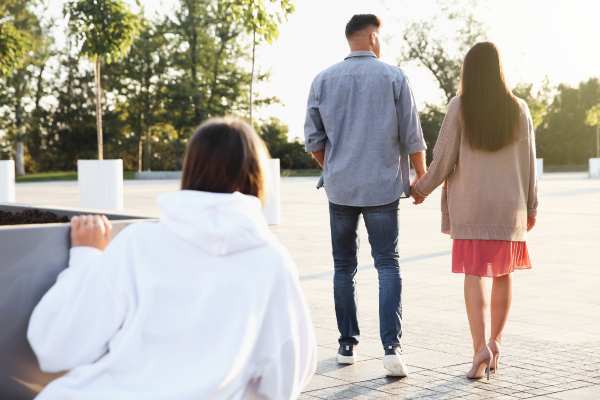 Foto de una pareja caminando y una mujer mirandolos a escondidad