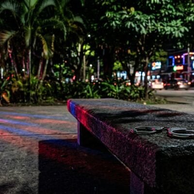 Esposas sobre una banca de concreto de noche con luces de policía al fondo