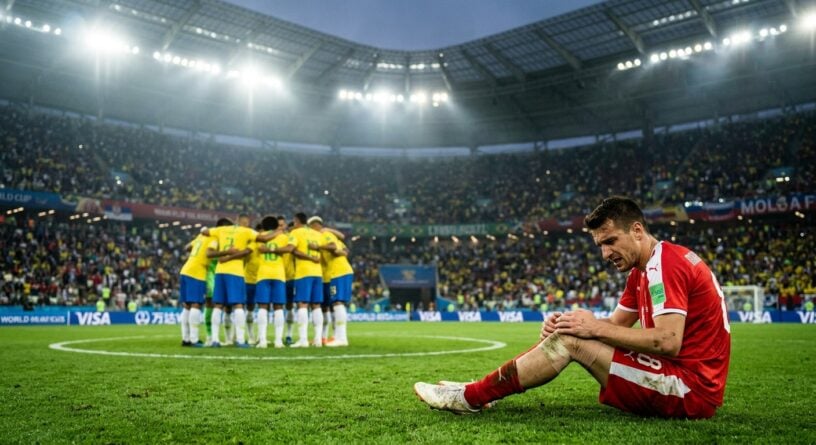 Un futbolista de rojo se lamenta sentado en el césped mientras el equipo rival de amarillo celebra al fondo